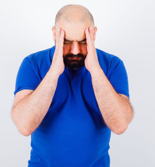 young male rubbing his temples in t-shirt and looking exhausted , front view.